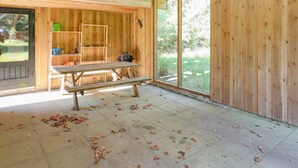 A wooden cabin interior with a picnic table, shelves, and a large window.