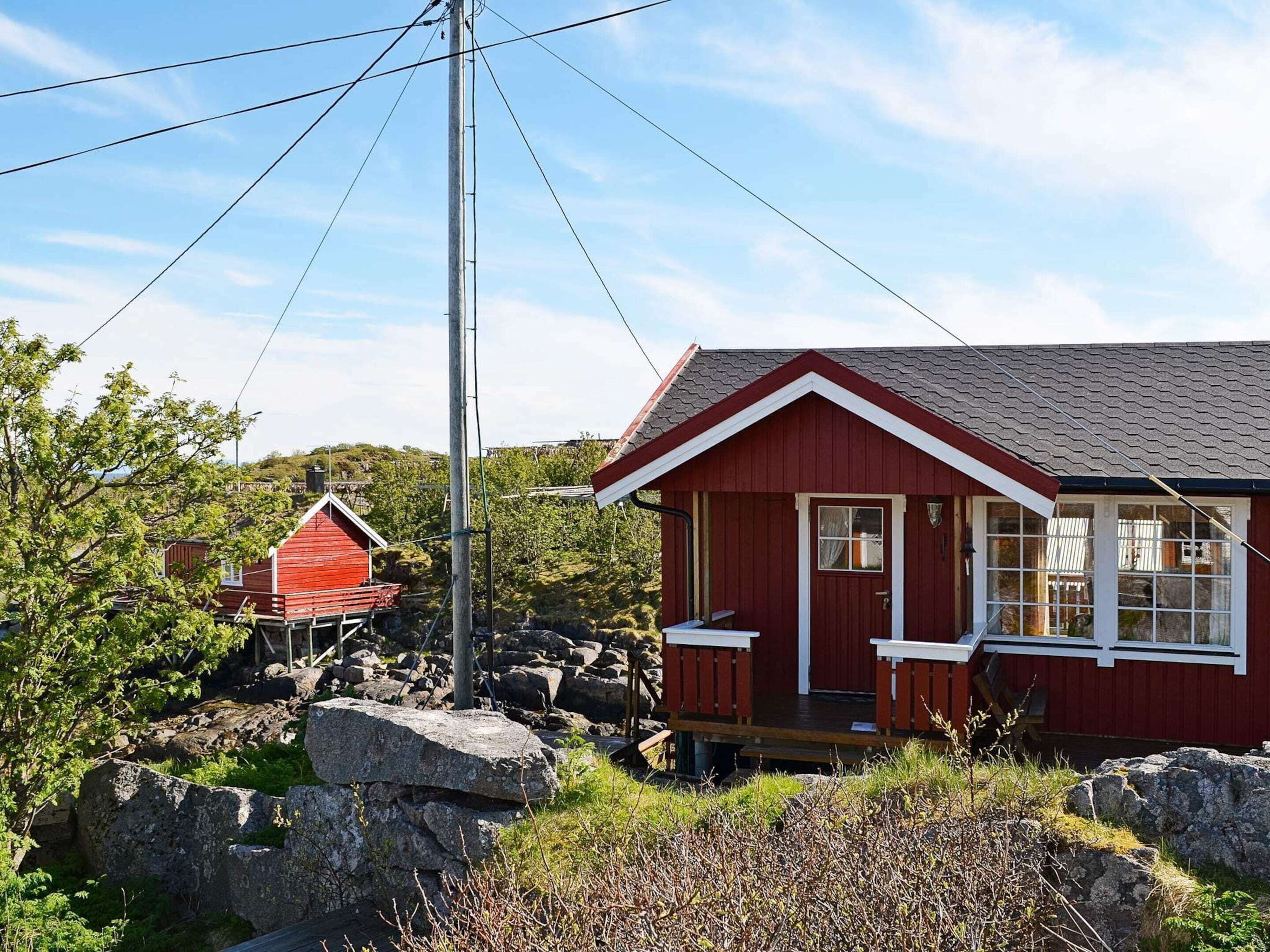 A red cabin with a white door and windows, surrounded by rocks and greenery.