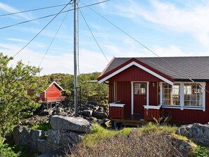 A red cabin with a white door and windows, surrounded by rocks and greenery. - 3 Person Holiday Home in Henningsvaer (Vagan)