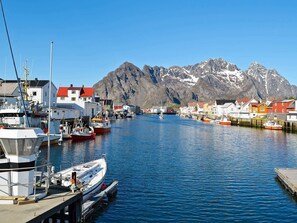 Un port où des bateaux sont amarrés, des bâtiments aux toits rouges et une montagne en arrière-plan.