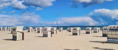 Ein Strand mit Reihen von Liegestühlen, die mit Nummern versehen sind, einem klaren Himmel und dem Meer im Hintergrund.