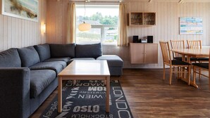 A cozy room with a sofa, a coffee table, a dining table with chairs, a cabinet with glassware, and a window with curtains. - Holiday Home in GrÃ¶mmitz (Groemitz)