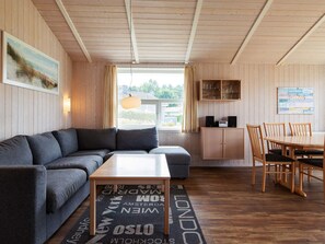 A cozy room with a sofa, a coffee table, a dining table with chairs, a cabinet with glassware, and a window with curtains.