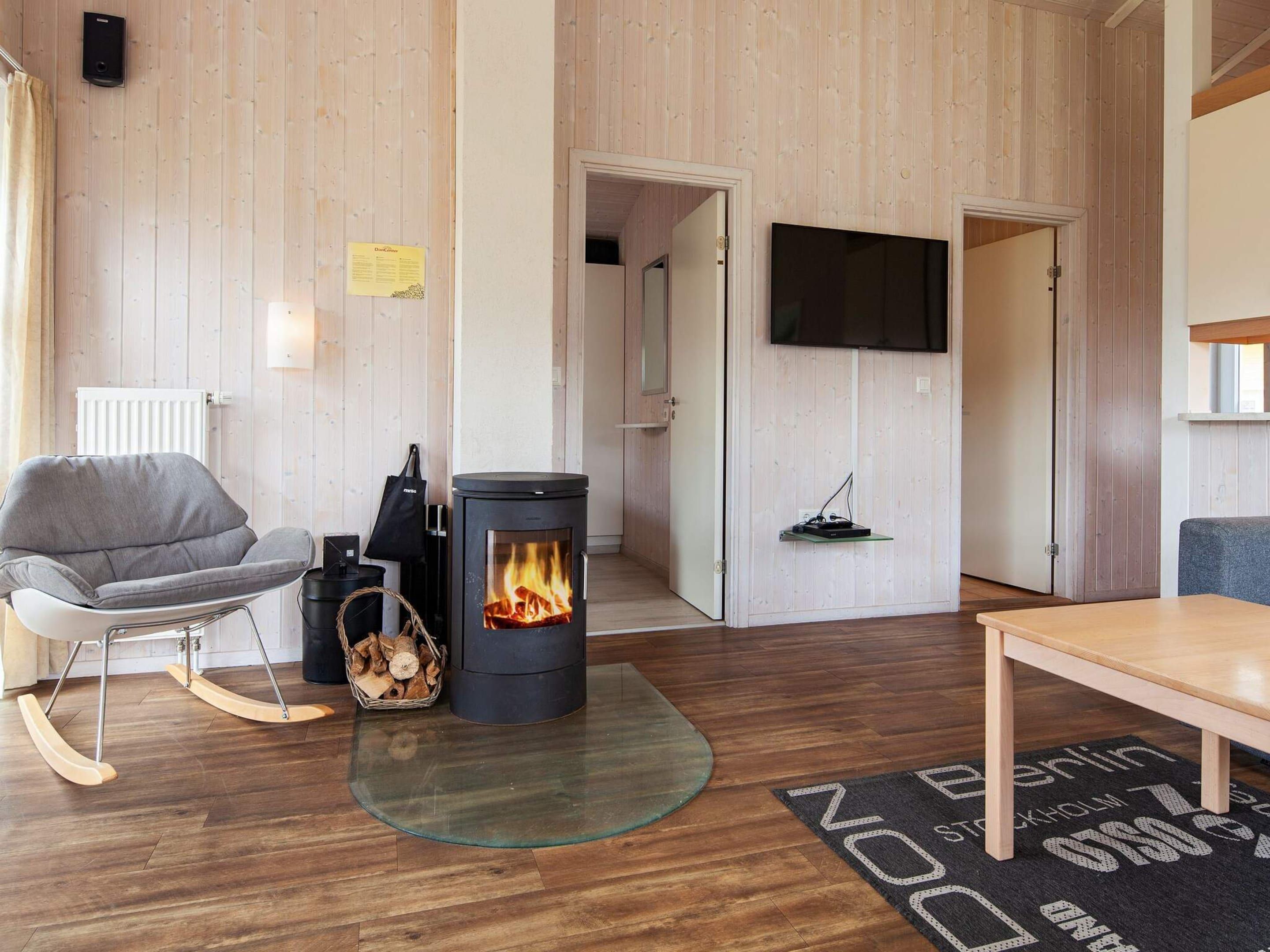 A cozy room with a wood-burning stove, a comfortable chair, a flat-screen TV, and a wooden floor.