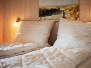 A bedroom with a wooden headboard, a bed with white bedding, and a wall-mounted light. - Holiday Home in GrÃ¶mmitz (Groemitz)