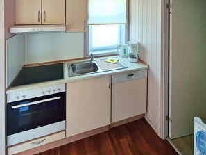 A compact kitchen with a built-in oven, a sink, and a window with blinds. - Holiday Home in GrÃ¶mmitz (Groemitz)