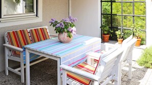 A patio with a striped table and white chairs, a vase with flowers, and a view through a window. - 3 Person Holiday Home in Hollviken-by Traum (Hollviken)