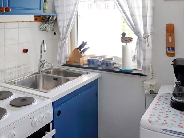 A kitchen with a white stove, a sink, and blue cabinets. There are two blue and white cups on the windowsill. - 3 Person Holiday Home in Hollviken-by Traum (Hollviken)