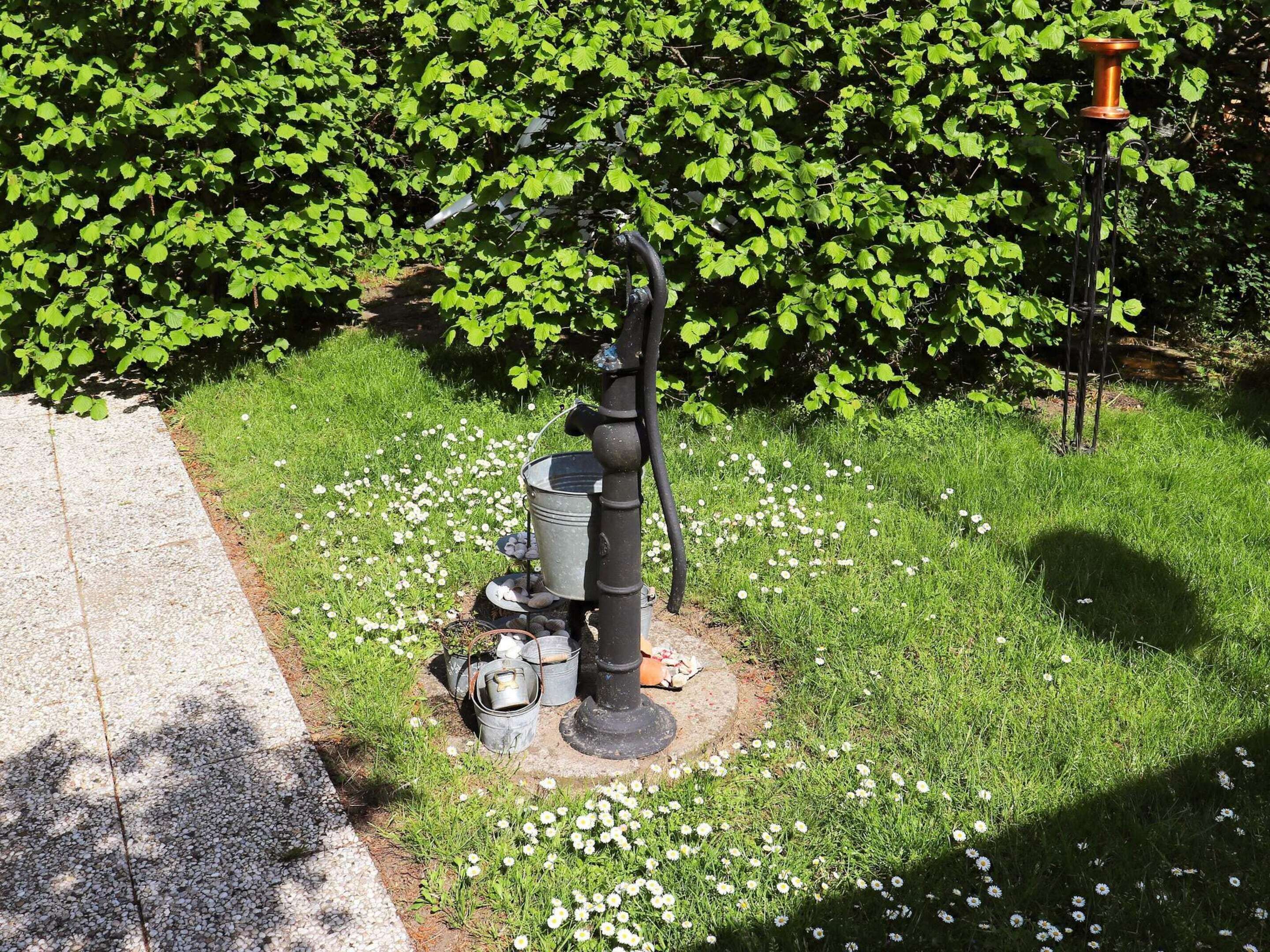 A garden with a metal sculpture, a metal bucket, and a metal container on the ground.