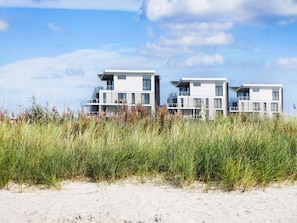 A modern beachfront property with multiple levels and balconies, surrounded by tall grasses and a clear sky. - Holiday Home in Wendtorf (Schönberg)