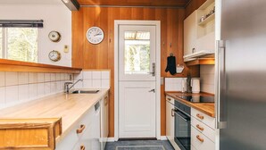 Une cuisine compacte avec des meubles en bois, un réfrigérateur en acier inoxydable et une fenêtre donnant sur les arbres.