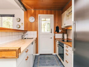 Een kleine keuken met houten kastjes, een roestvrijstalen koelkast en een raam met uitzicht op bomen.