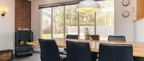 A dining area with a wooden table and black chairs, a brick fireplace, and a large window with a view of the outdoors.