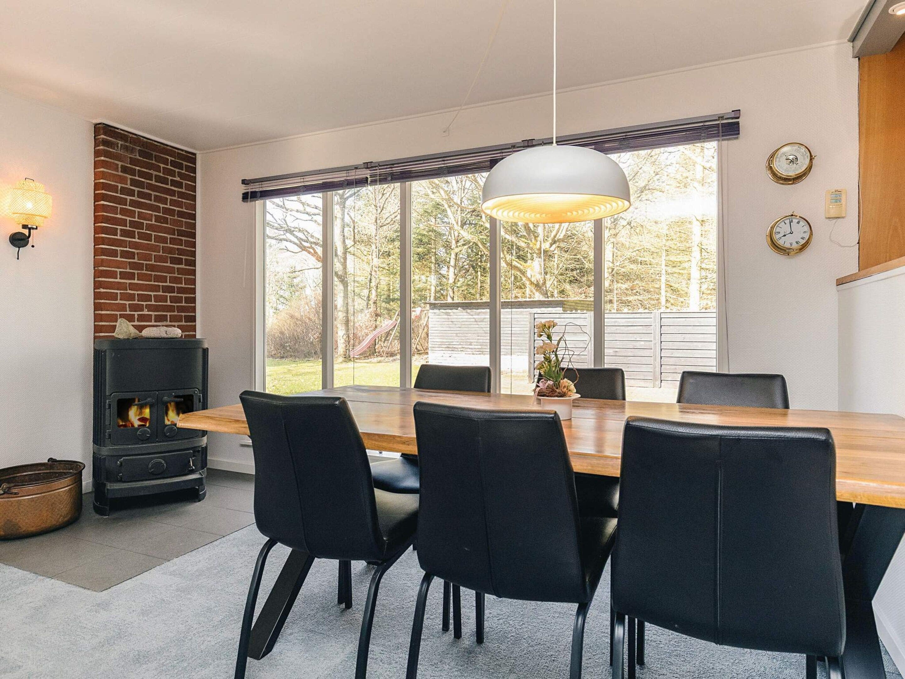 Una cocina moderna con un amplio ventanal, pared de ladrillo, estufa de leña y comedor con sillas y mesa.