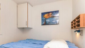 Een slaapkamer met een bed, een wit kastje, een schilderij en een houten plankunit.