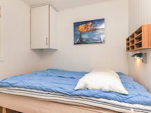 Een slaapkamer met een bed, een wit kastje, een schilderij en een houten plankunit.