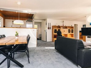 Una sala de estar moderna con comedor, un sofá de cuero negro, armarios de madera y un televisor de pantalla plana.