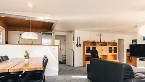 Een moderne woonruimte met een eethoek, een zwarte leren bank en een keuken met houten kastjes en een televisie.