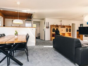 Een moderne woonruimte met een eethoek, een zwarte leren bank en een keuken met houten kastjes en een televisie.