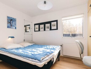 Un dormitorio con cama, una silla, un ventanal y obras de arte en la pared.