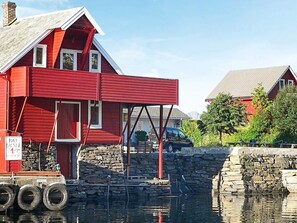 Une maison rouge avec une jetée en pierre qui s’avance dans un plan d’eau.