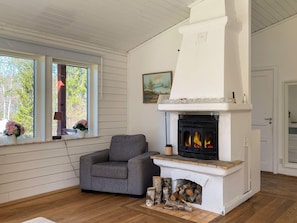 Una habitación con chimenea, un sillón gris, suelo de madera y ventana con vistas a árboles.