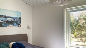 Ein Schlafzimmer mit einem Bett, einem Gemälde eines Hafens, einem Fenster mit Blick auf Bäume und einer Deckenleuchte.
