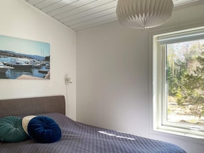 Um quarto com uma cama, um quadro de um porto, uma janela com vista para árvores e um lustre no teto.