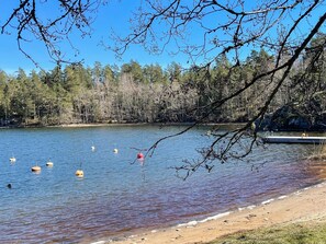Un lac parsemé de bouées flottantes, avec un quai et une rive bordée d’arbres.