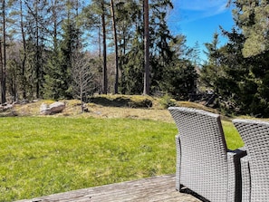 A deck with wicker furniture, a grassy lawn, and a forested backdrop. - 3 Person Holiday Home in Norrtalje (Norrtälje)