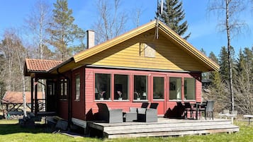 A red wooden cabin with a yellow roof, large windows, and a porch with outdoor furniture.
