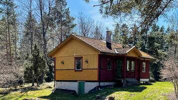 A two-story wooden house with a red door and yellow siding, surrounded by a forested area.