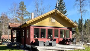 A red wooden cabin with a yellow roof, large windows, and a porch with outdoor furniture.