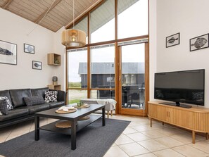 En moderne stue med en sort lædersofa, et sofabord, et fjernsyn og store vinduer.