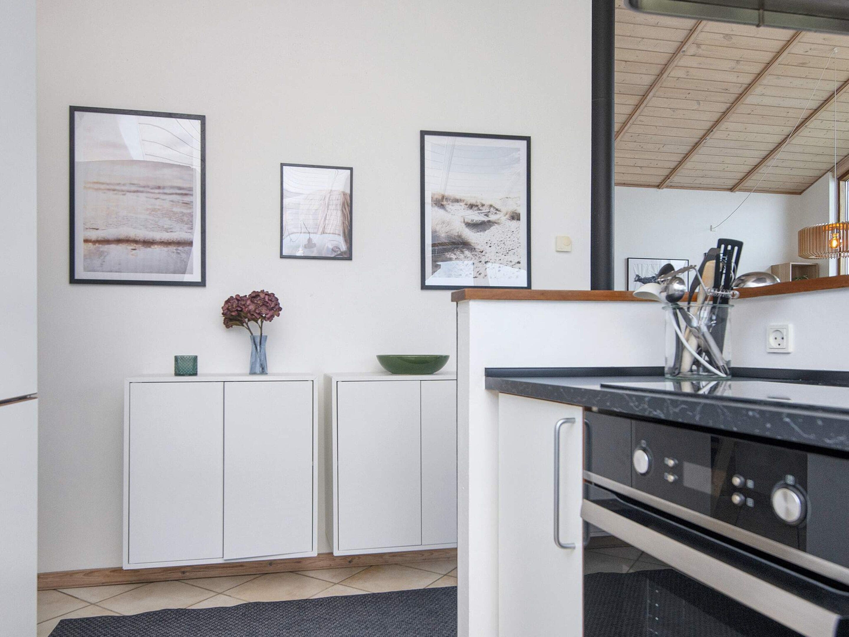 Una cocina moderna con armarios blancos, encimera negra y electrodomésticos de acero inoxidable. Hay cuadros en la pared y un jarrón con flores sobre la encimera.