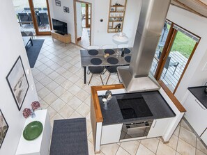 A modern kitchen with a central island, a dining area with a round table, and a view of the outdoors through large windows.