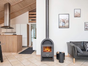 A modern living room with a fireplace, a sofa, and a kitchen area with cabinets and a chimney.