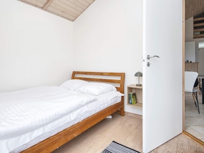 Una cama individual con cabecera de madera en una habitación con paredes blancas y techo de madera.