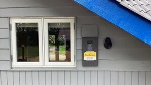 A building with a grey siding exterior, a double door window, and a utility box with a sign. - 4 Star Holiday Home in Ansager (Ansager)
