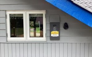 A building with a grey siding exterior, a double door window, and a utility box with a sign.