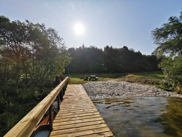 A wooden boardwalk leading to a picnic table by a river, surrounded by trees.