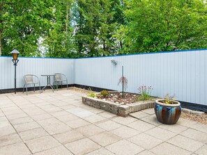 A patio with a blue fence, two chairs, a table, and a potted plant.