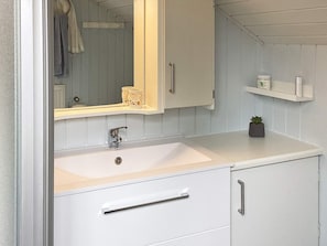 A bathroom with a white sink, a mirror, a cabinet, and a shelf with toiletries.