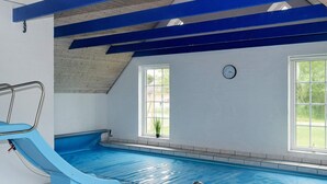 An indoor swimming pool with a blue slide, clear windows, and a clock on the wall. - Tranquil Holiday Home in Ulfborg With Sauna (Ulfborg)