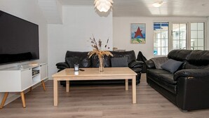 A modern living room with a flat-screen TV, a wooden coffee table, two black leather sofas, and a large window with a view of the outside. - Tranquil Holiday Home in Ulfborg With Sauna (Ulfborg)