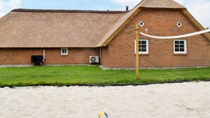 A beach house with a thatched roof, brick walls, and a sandy beach in front. - Tranquil Holiday Home in Ulfborg With Sauna (Ulfborg)
