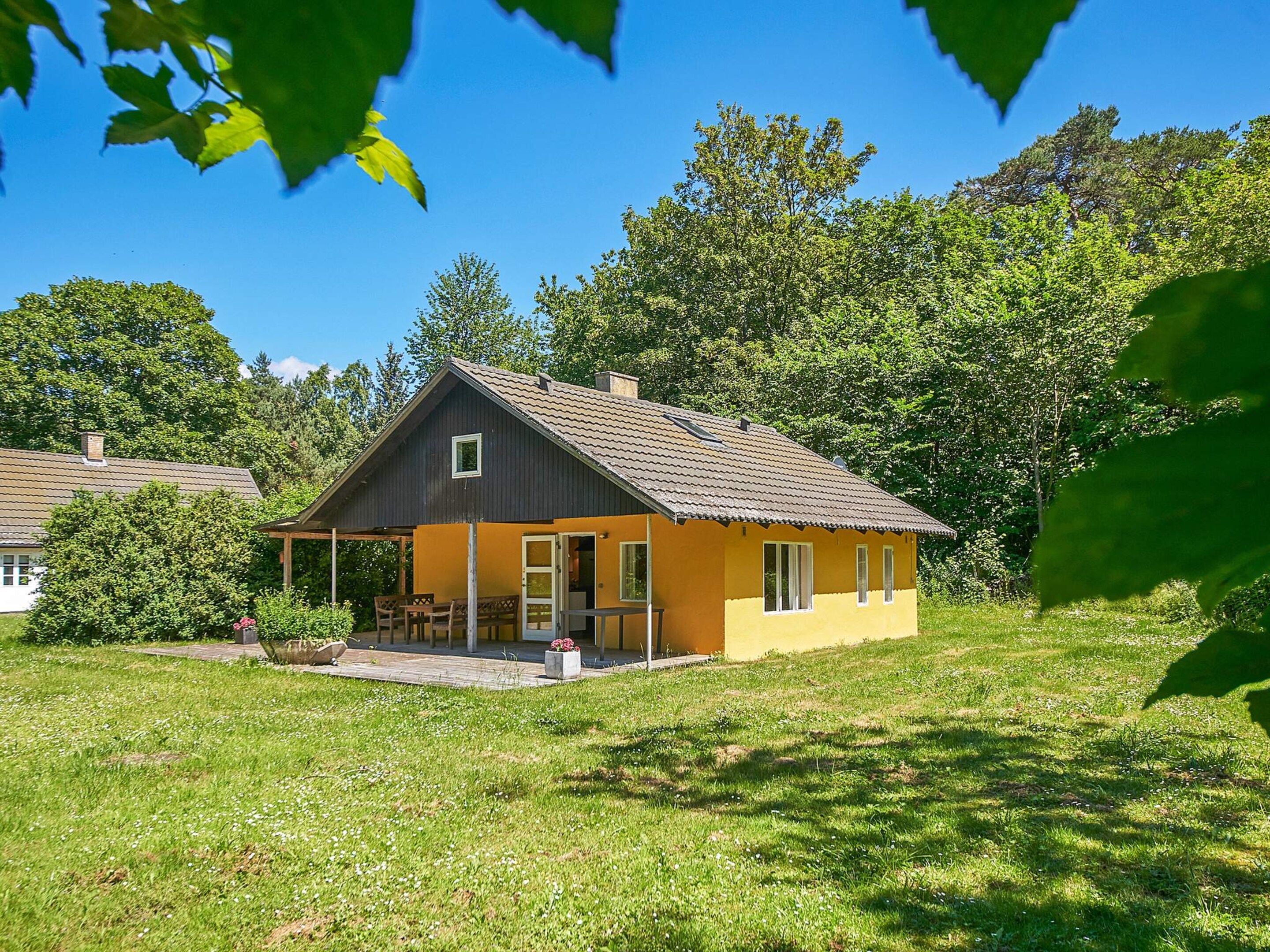 A single-story house with a porch, surrounded by a grassy yard and trees.