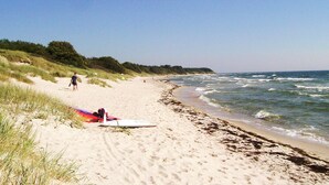 A sandy beach with waves, a tent, and a person lying on the sand. - 6 Person Holiday Home in Aakirkeby (Akirkeby)