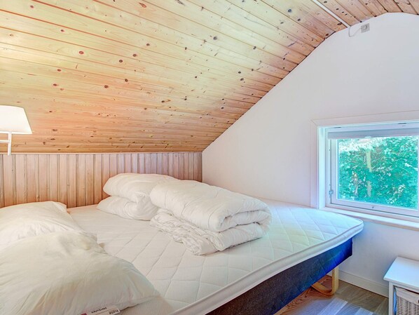 A bedroom with a sloped ceiling, a bed with white bedding, a window with a view of greenery, and a small bedside table. - 6 Person Holiday Home in Aakirkeby (Akirkeby)