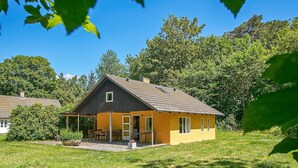 A single-story house with a porch, surrounded by a grassy yard and trees. - 6 Person Holiday Home in Aakirkeby (Akirkeby)